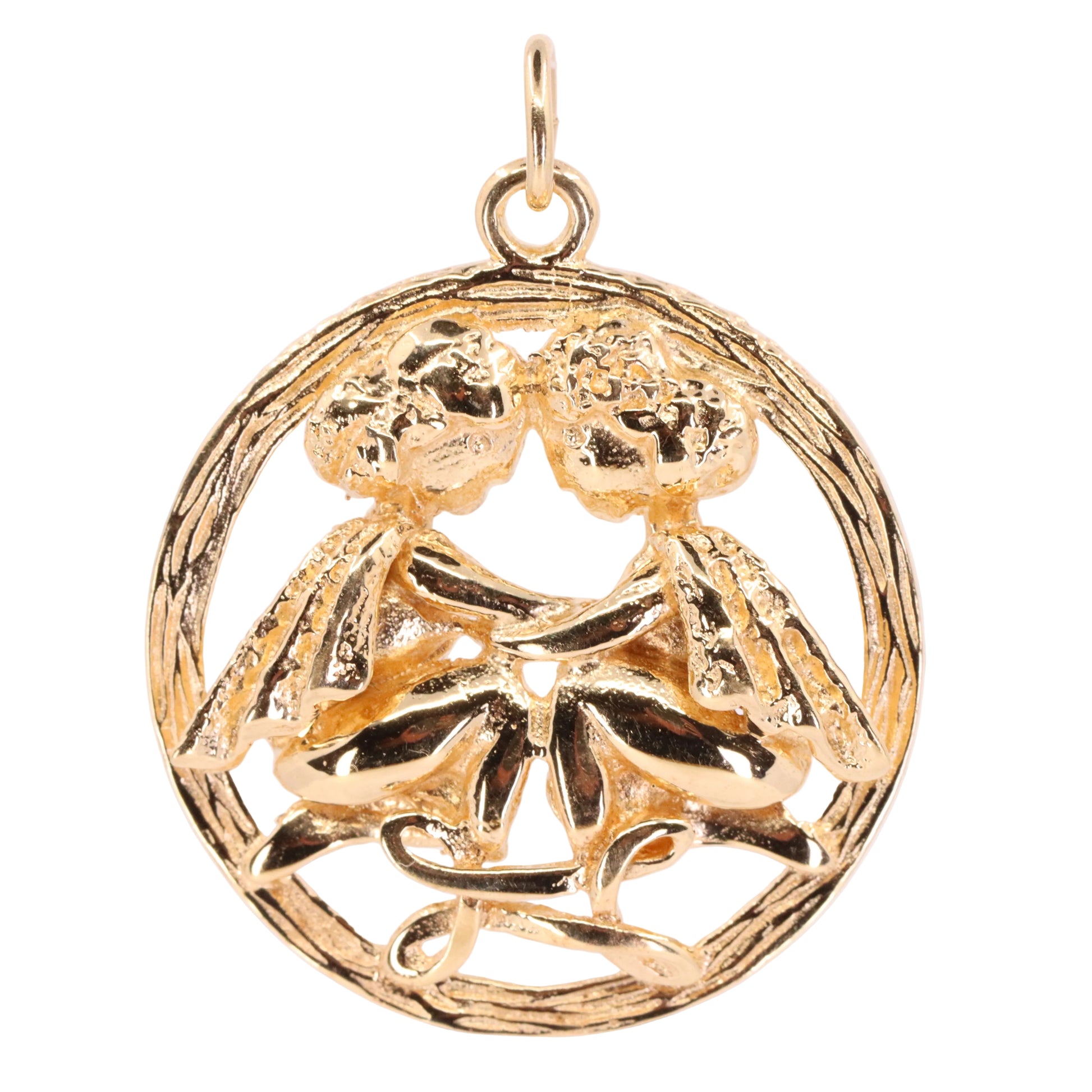 A gold pendant charm featuring a circular design with two stylized figures embracing, set against a plain light background.