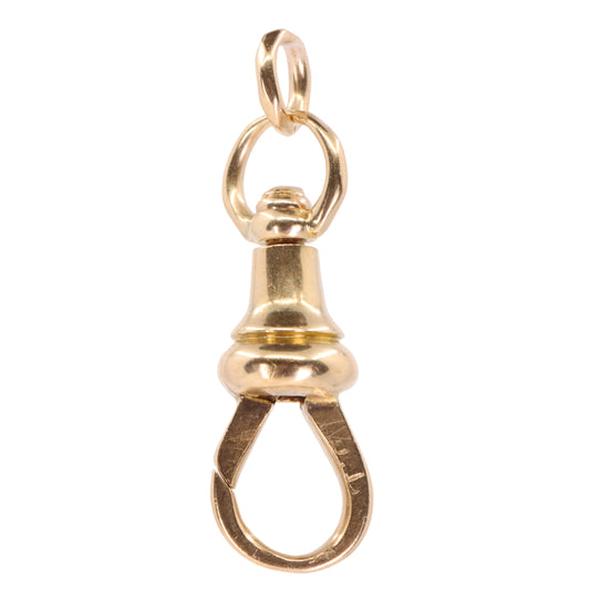 A polished gold-tone clasp charm pendant with a top loop and a teardrop-shaped bottom clasp, shown against a plain light pink background.